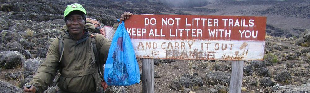 SENE mountain guide picking up litter on Kilimanjaro next to a sign:"keep all litter with you"